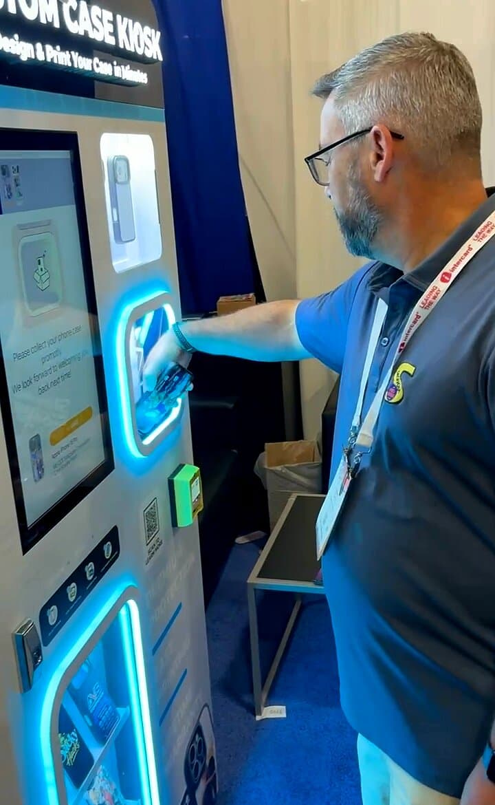 An attendee collecting his freshly printed phone case from the kiosk's glowing pickup slot