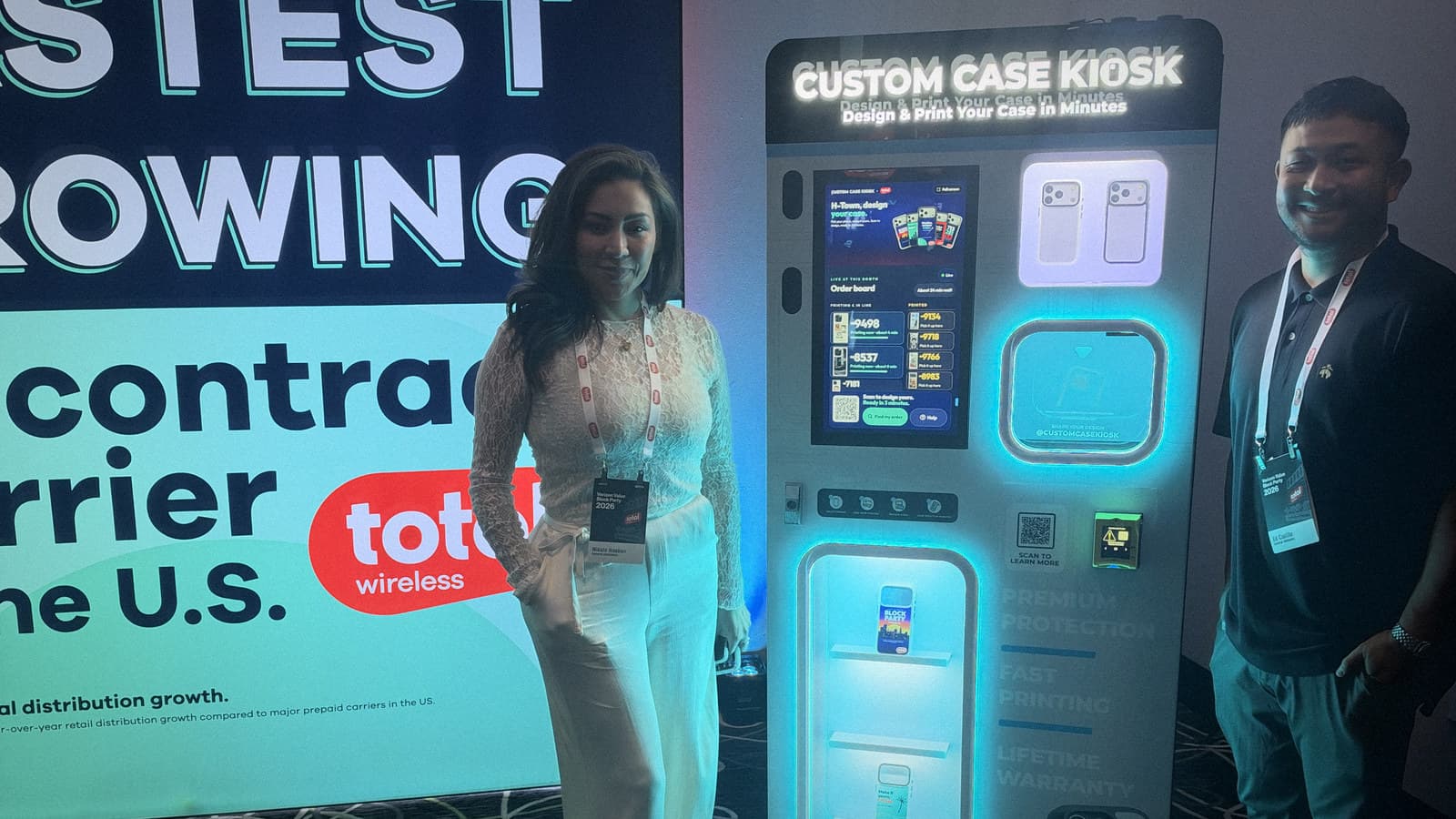 Two team members standing beside the lit Custom Case Kiosk in front of the Total Wireless wall at the Katy, Texas Block Party.