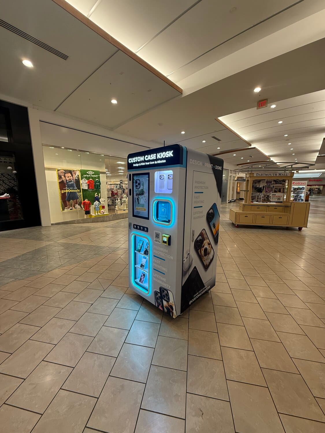 Custom Case Kiosk at Dartmouth Mall — side panel with Design, Print, Done graphics and the mall directory behind