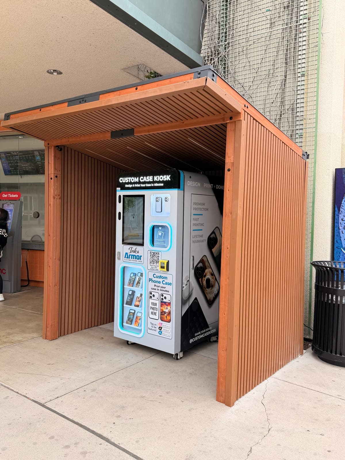Custom Case Kiosk at The Outlets at Orange in Orange, CA — the kiosk inside its open-air wood-slatted shelter on the walkway beside the AMC theatre