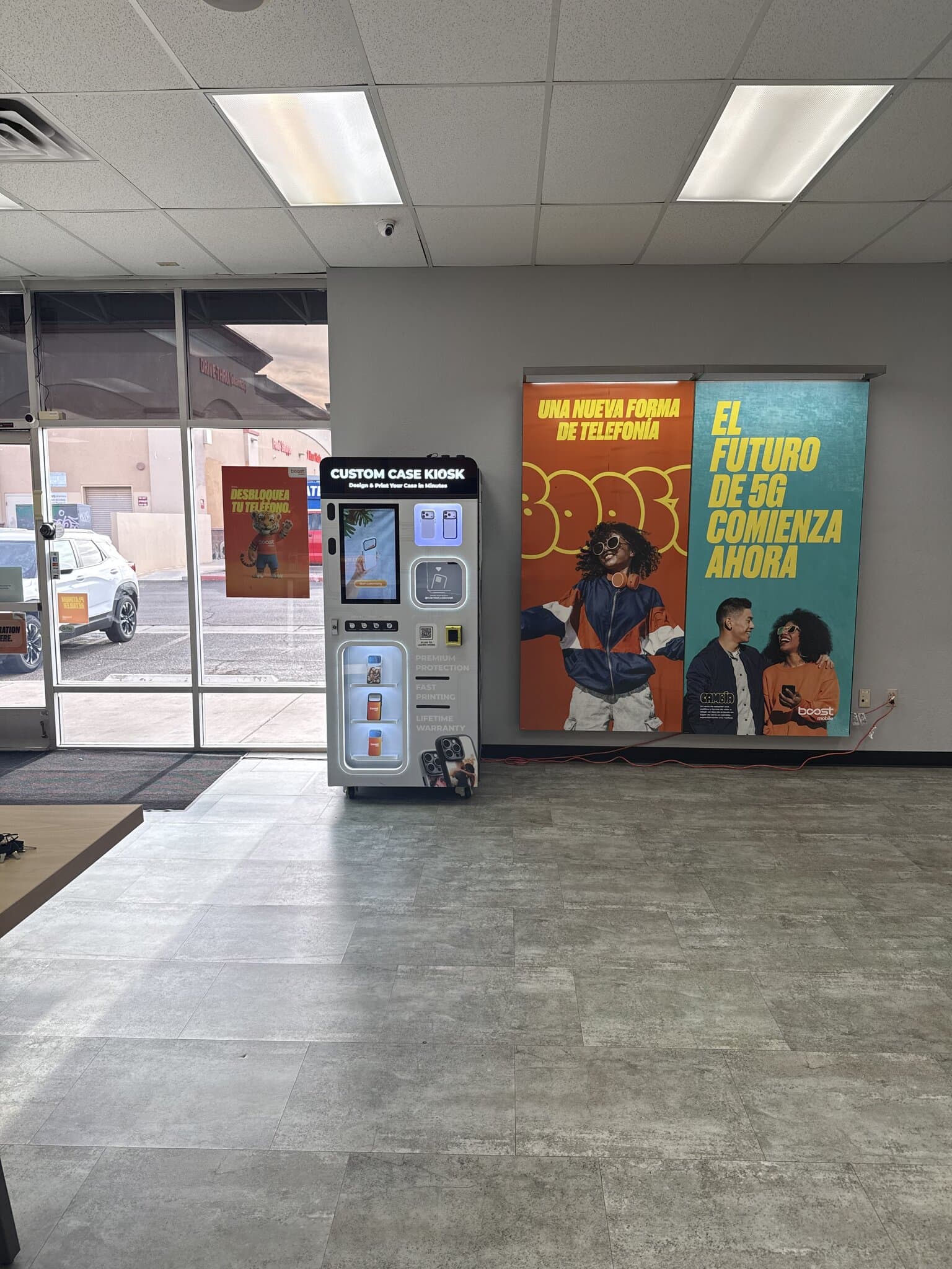 Custom Case Kiosk against the Boost Mobile banner wall inside the store on W Indian School Rd in Phoenix, AZ — lit design touchscreen and backlit case shelves