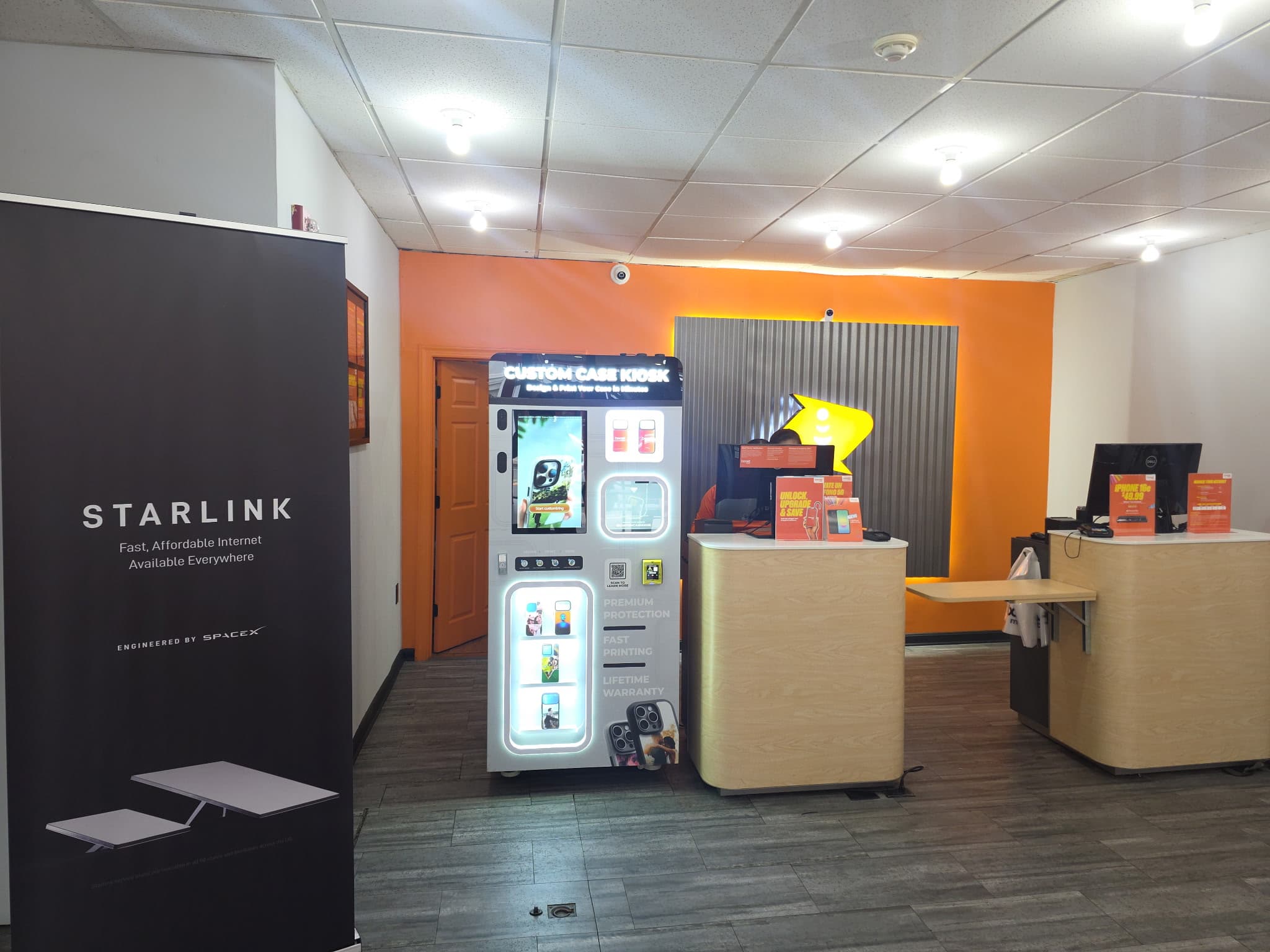 Inside the Boost Mobile store in Riverside, NJ — the Custom Case Kiosk against the orange feature wall beside the service counters